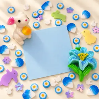 Illustrative blank craft card surrounded by blue daisy pieces, a rabbit charm and a blue flower charm