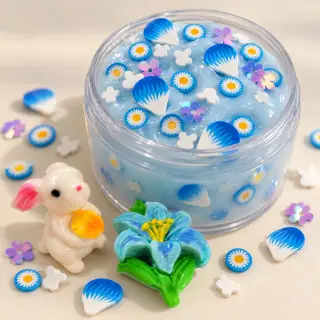 Illustrative blue slime jar with daisy fillers and rabbit and flower focal charms beside it