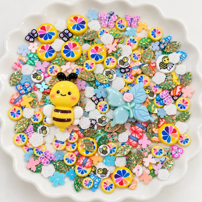 Studio overview of yellow bee and blue flower-like charms among rainbow roundels and small botanical pieces