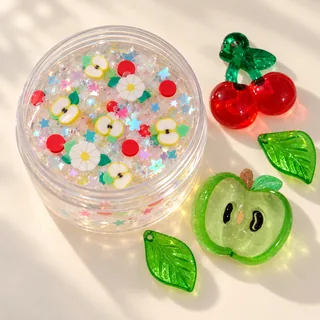 Illustrative clear slime jar with small apple and daisy pieces while resin focal charms rest outside