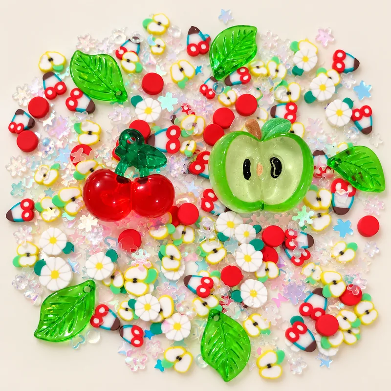 Studio overview of cherry and green apple resin charms with daisies, green leaves and small fruit pieces