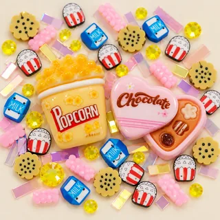 Close view of yellow popcorn-carton and pink heart chocolate-box resin focal charms amid snack motifs