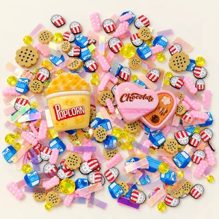 Studio overview of popcorn-carton and pink heart chocolate-box charms with small popcorn, milk and cookie pieces