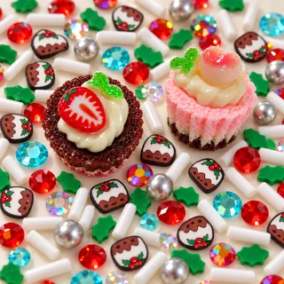 Close detail of strawberry tart and pink cupcake resin focal charms beside small holiday pudding slices