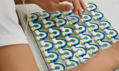 Hands arranging dimensional rainbow decorations on a tray; a separate design reference
