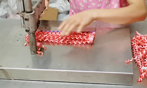 Worker guiding red-and-white patterned clay canes at a cutting machine