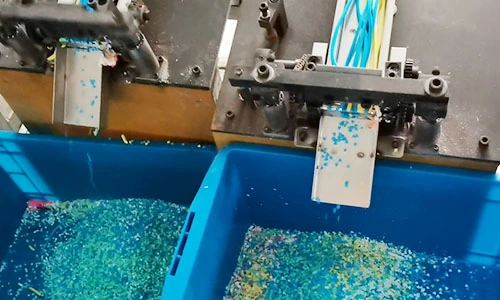 Cutting machines feeding small blue and yellow patterned slices into blue collection bins