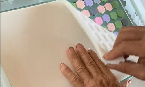 Hands peeling back a flexible mould containing pastel flower-shaped resin charms