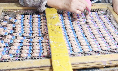Worker adding fine details to small character-shaped decorative charms on mesh trays