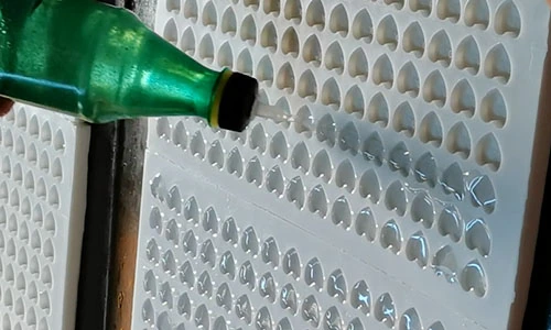 Liquid being poured from a green bottle into a mould with heart-shaped cavities