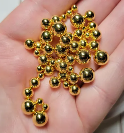 Original hand-held close-up of metallic gold round no-hole faux pearl beads