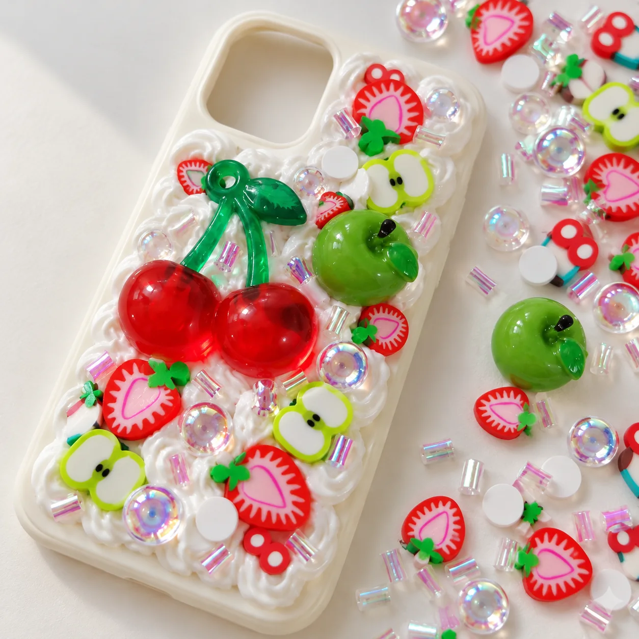 Illustrative cream-glue phone case with cherry and apple themed craft fillers